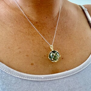 May include: A silver chain necklace with a green gemstone pendant encased in a gold wire cage.