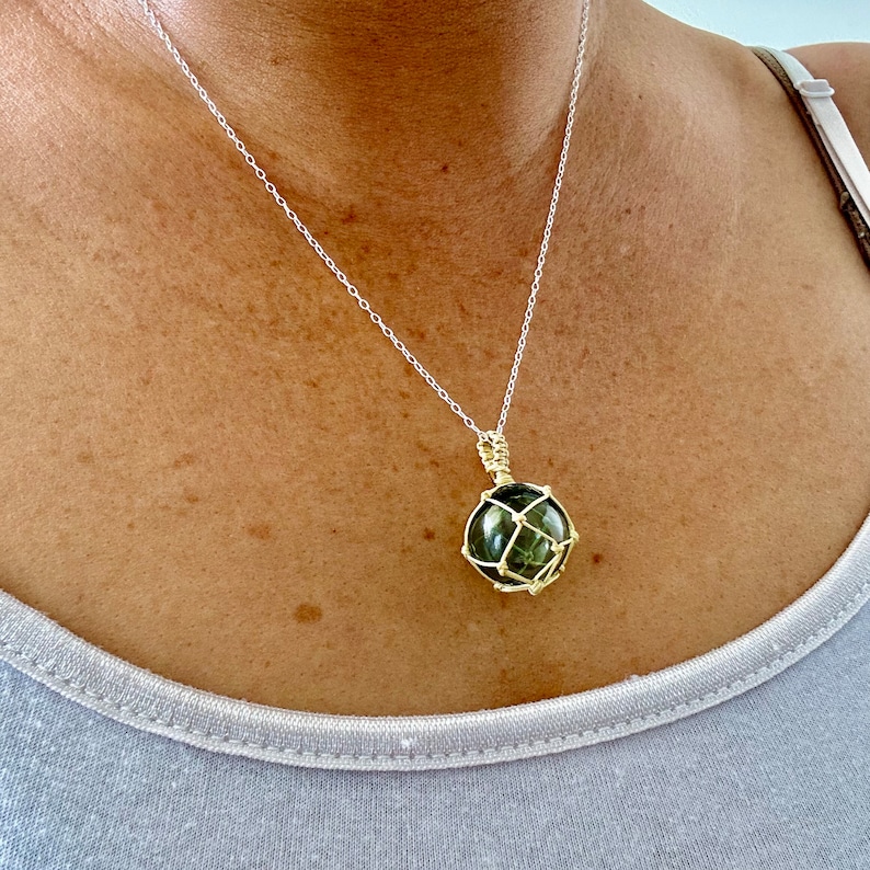 May include: A silver chain necklace with a green gemstone pendant encased in a gold wire cage.