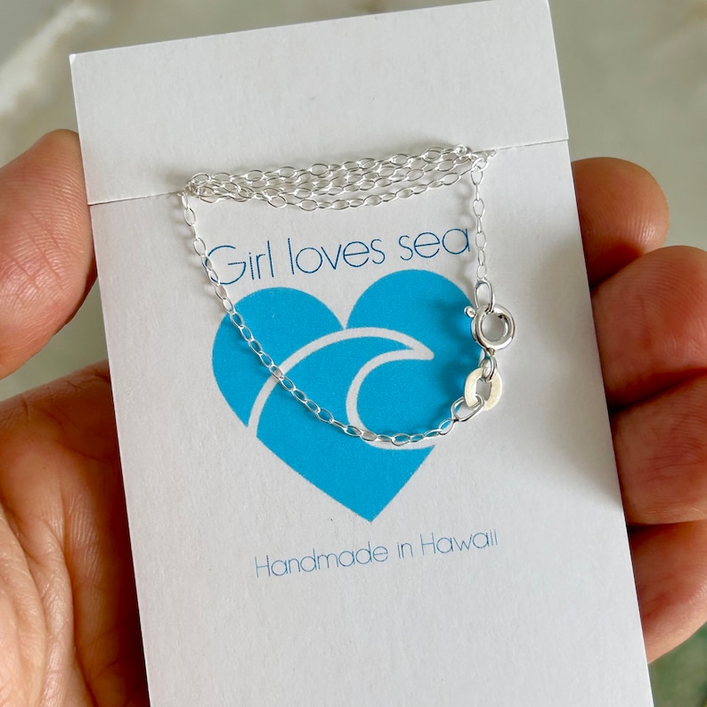 May include: A silver chain necklace with a lobster clasp. The necklace is on a white card with the text "Girl loves sea" and "Handmade in Hawaii".