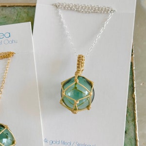 May include: A gold-filled necklace with a sterling silver chain and a green glass float pendant wrapped in a gold-colored cord.