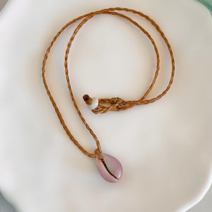 May include: A pink seashell pendant necklace with a brown braided cord and a white bead.