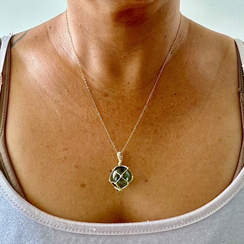 May include: A gold chain necklace with a green gemstone pendant encased in a gold wire cage.