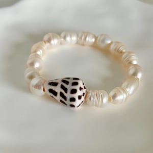 May include: A white pearl bracelet with a brown and white seashell charm.