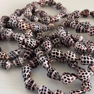 Peut inclure: Collier de coquillages naturels avec un motif tachet&eacute; noir et blanc. Les coquillages, de couleur beige ros&eacute; clair, sont enfil&eacute;s, sugg&eacute;rant un collier ou un bracelet.