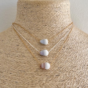 Peut inclure: Trois colliers en or avec des pendentifs en coquillage blanc et gris. Les colliers sont superposés sur un mannequin en paille.