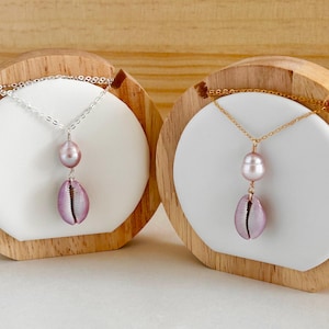 May include: Two necklaces with a pink shell pendant and a pink pearl. One necklace has a silver chain and the other has a gold chain.