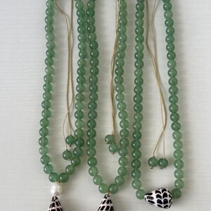 May include: Three green beaded necklaces with seashell pendants. The necklaces have a light green hue and are strung with small, round beads. Each necklace features a different seashell pendant, with one featuring a white pearl.