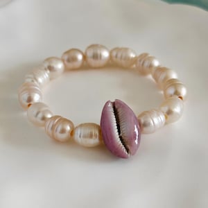 May include: A bracelet made of white and cream pearls with a purple cowrie shell charm.