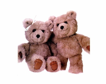 May include: Two brown teddy bears sitting side by side. The bear on the left has a white bow on its head. Both bears have brown eyes and noses.