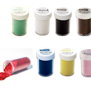 May include: An assortment of eight small, clear plastic jars with white lids, filled with colorful glitter. Colors include green, white, black, brown, red, blue, yellow, and pink. One jar is tipped over, spilling red glitter.