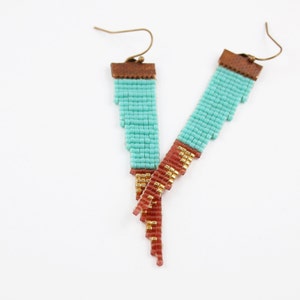 May include: A pair of turquoise and gold beaded earrings with a brown leather accent. The earrings are dangle style and have a long, cascading design.
