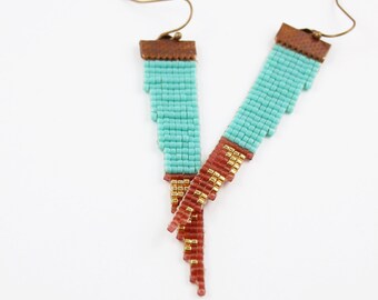 May include: A pair of turquoise and gold beaded earrings with a brown leather accent. The earrings are dangle style and have a long, cascading design.