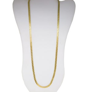 May include: A gold-colored herringbone chain necklace displayed on a white mannequin. The necklace has a flat, zig-zag pattern and hangs vertically. The chain is a warm, metallic tone.