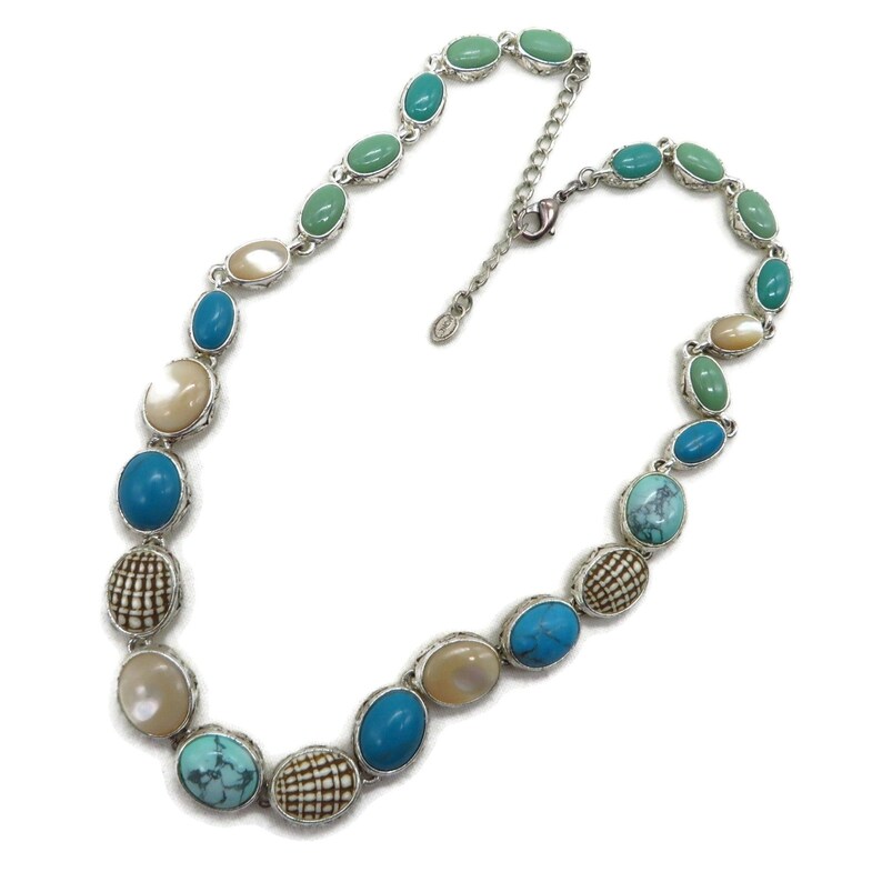 A silver-tone necklace with alternating oval and round beads in turquoise, cream, and brown, laid flat in a full circle with an extender chain visible on a white background.
