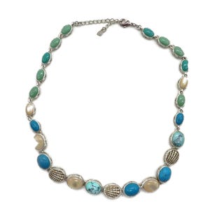 A silver-tone necklace with alternating oval and round beads in turquoise, cream, and brown, laid flat in a full circle on a white background.