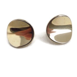 May include: A pair of gold-toned stud earrings featuring a smooth, circular, and slightly concave design. The polished metal surface reflects light, creating a bright, metallic appearance on each of the two round earring pieces.