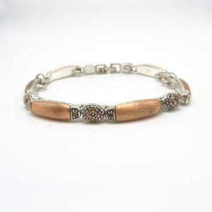 May include: A silver-toned link bracelet featuring alternating smooth, matte copper-coloured cylindrical segments and small, oval-shaped silver links encrusted with tiny, sparkling amber-coloured stones. The bracelet includes a secure metal clasp.