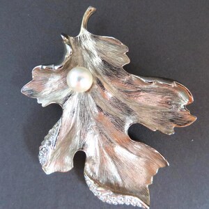 May include: Silver-toned leaf-shaped brooch with a central pearl and rhinestone accents. The brooch has a textured surface, and the leaf design is detailed with veining. A classic accessory.