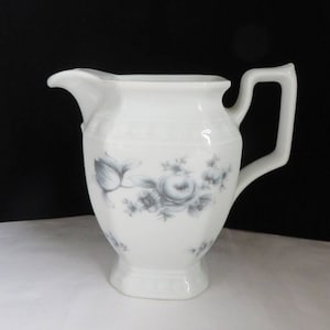 May include: White ceramic creamer with a gray floral design. The creamer has a spout, a handle, and a decorative floral pattern. The creamer is a classic design, suitable for serving cream or milk.