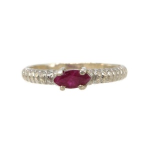 May include: A silver ring with a textured band and a marquise-cut ruby gemstone. The ruby is a deep red color and is set in a four-prong setting. The ring is a delicate piece of jewelry.