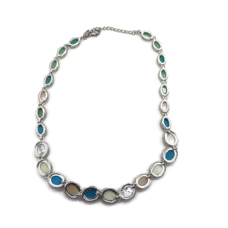 The back of a silver-tone necklace with alternating oval and round beads in turquoise, cream, and brown, laid flat in a full circle on a white background.