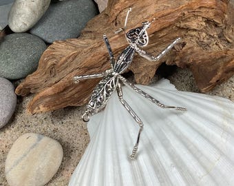 May include: A silver praying mantis sculpture with intricate details, posed on a white seashell. The sculpture is made of wire and beads, and has a delicate, airy feel.