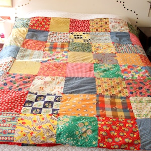 May include: A patchwork quilt with a variety of colorful fabric squares. The quilt features red, yellow, blue, and green patterns, including floral, geometric, and animal prints. The quilt is spread over a bed.