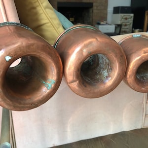 May include: Three copper kitchen tools with a green patina. The tools are round and have a large opening in the center. They are arranged in a row from largest to smallest.