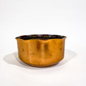 May include: A copper bowl with a dark, wavy rim. The bowl has a rounded shape and a smooth, polished surface. The copper has a warm, reddish-brown hue, and the bowl appears to be vintage or antique.