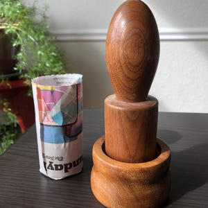 May include: A wooden mortar and pestle set. The mortar is a brown cylinder with a rounded base. The pestle is a brown oval shape with a smooth surface.