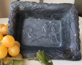 Puede incluir: Una bandeja rectangular negra con un diseño de dragón en relieve alrededor del borde. La bandeja tiene una escena tallada de personas en una habitación con una grúa.