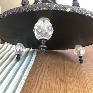 May include: Black metal base with three crystal feet. The base has a decorative, ornate design around the edge.