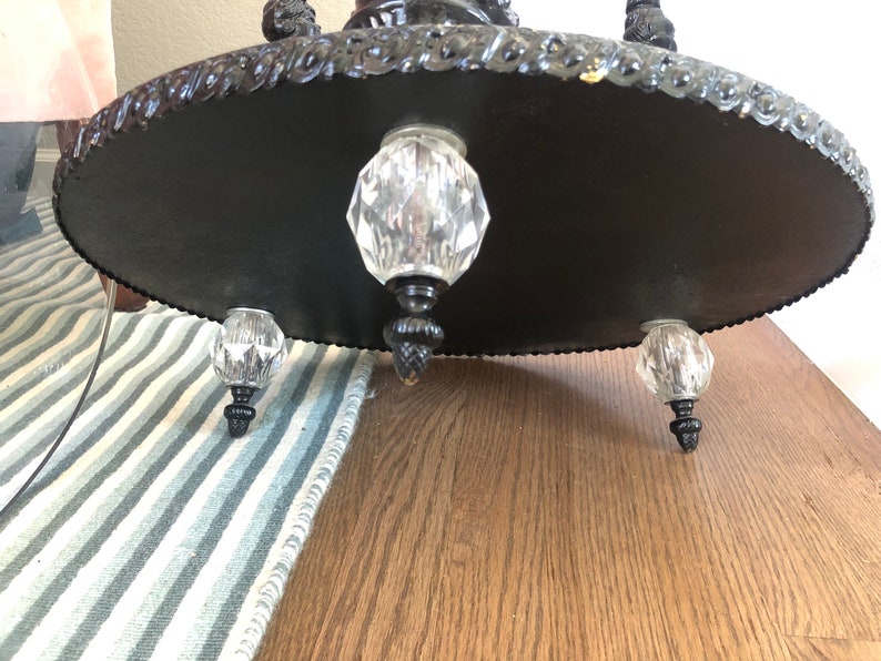 May include: Black metal base with three crystal feet. The base has a decorative, ornate design around the edge.