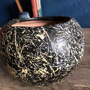 May include: Black ceramic planter with a white crackle glaze. The planter is round and has a wide opening.