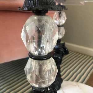 May include: Close-up of a black and clear glass table base with a crystal ball design. The base is made of metal and has a decorative design. The table top is not visible in the image.