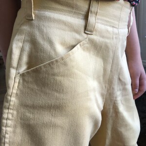 Op de afbeelding: Een lichtgele broek met hoge taille en een voorzak.
