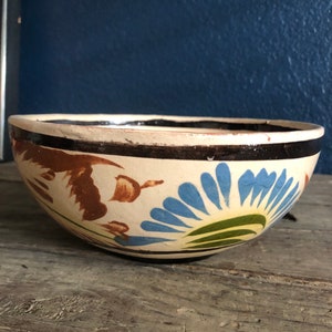 May include: A white ceramic bowl with a brown rim and painted blue, green, and brown floral designs.