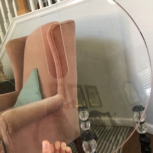 May include: A clear, round, acrylic table top with a unique cutout design. The table top is resting on three black metal legs with crystal accents.