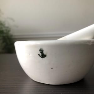 Puede incluir: Mortero y maja de cerámica blanca con un diseño de mano negra en el lateral del cuenco.