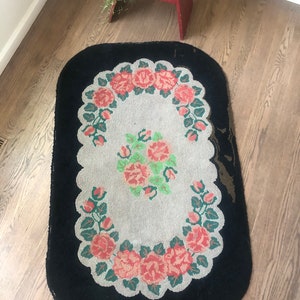 Puede incluir: Una alfombra ovalada vintage con un borde negro y un centro blanco con un dise&ntilde;o floral de rosas rosas y hojas verdes.