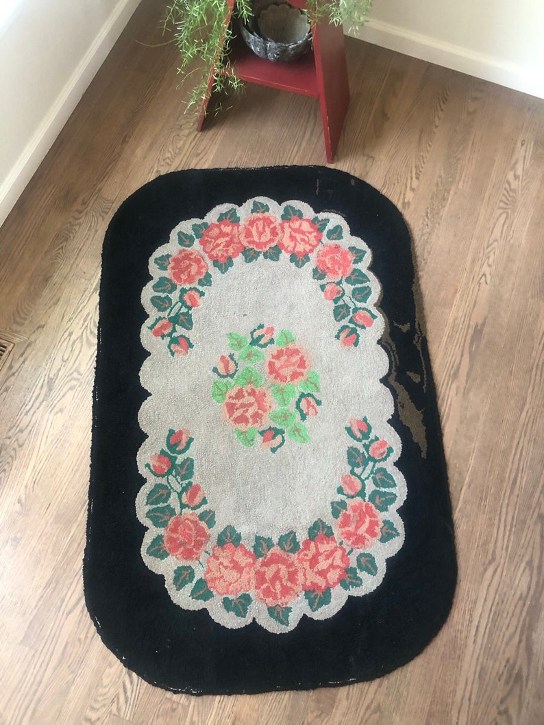 Puede incluir: Una alfombra ovalada vintage con un borde negro y un centro blanco con un dise&ntilde;o floral de rosas rosas y hojas verdes.