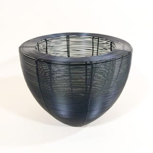 May include: A dark gray wire basket with a rounded, bowl-like shape. The basket is constructed from numerous horizontal wires, creating a textured surface. The open design allows for visibility of the interior.