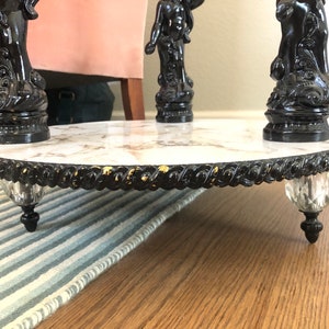 May include: A round marble table with a black and gold trim. The table has three black, ornate legs with crystal finials.