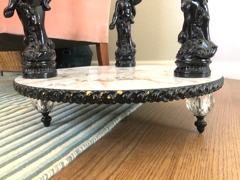 May include: A round marble table with a black and gold trim. The table has three black, ornate legs with crystal finials.