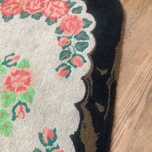 Puede incluir: Una alfombra ovalada blanca con un borde negro y un dise&ntilde;o floral con rosas rosas y hojas verdes.