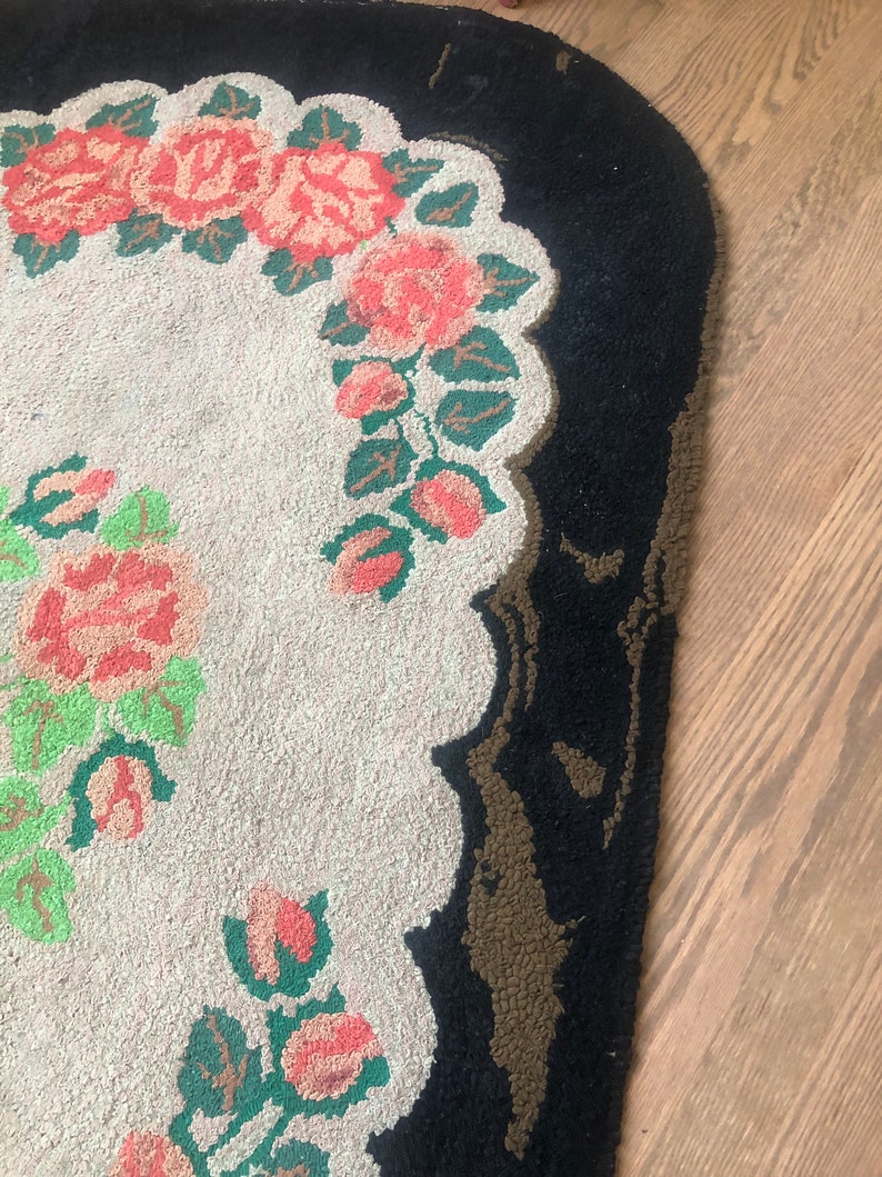 Puede incluir: Una alfombra ovalada blanca con un borde negro y un dise&ntilde;o floral con rosas rosas y hojas verdes.