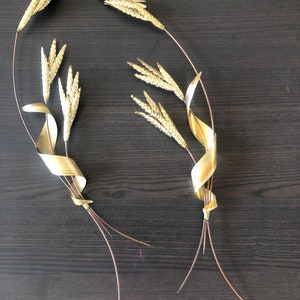 May include: Two gold metal wall sculptures of wheat stalks with twisted stems. The sculptures are made of thin metal and have a realistic appearance.