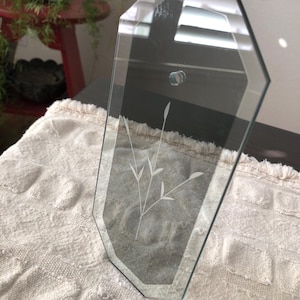 May include: A clear glass picture frame with a beveled edge and an etched floral design. The frame is octagonal in shape and has a silver finish.