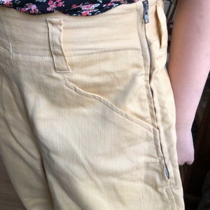 Op de afbeelding: Een lichtgele broek met een hoge taille en een rits aan de zijnaad. De broek heeft een klassieke, rechte pasvorm en is gemaakt van een zachte, gestructureerde stof.