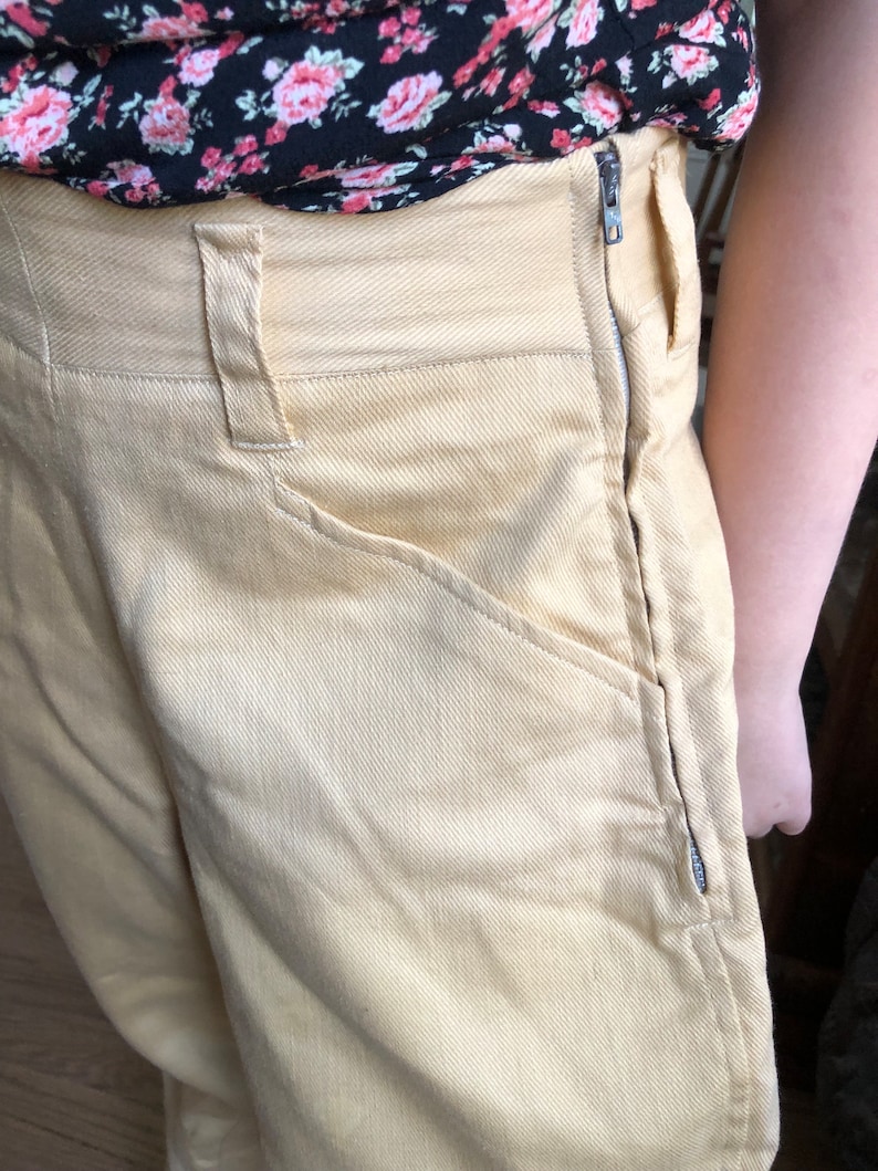 Op de afbeelding: Een lichtgele broek met een hoge taille en een rits aan de zijnaad. De broek heeft een klassieke, rechte pasvorm en is gemaakt van een zachte, gestructureerde stof.